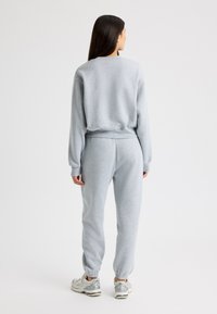 Sudadera de algodón gris con puños de canalé, combinada con joggers a juego. Presenta dobladillos elásticos y un corte relajado. Zapatillas deportivas completan el look.