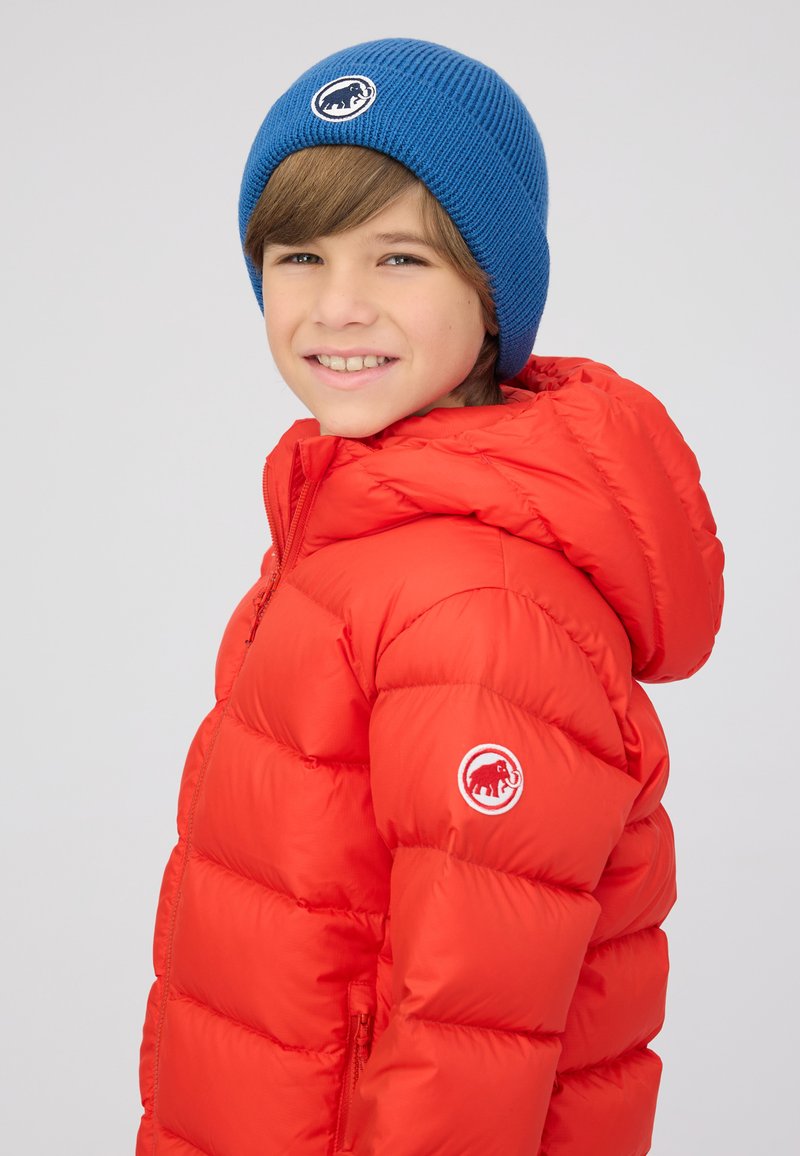 Rood donzen jack met capuchon, met een diagonaal gewatteerd ontwerp en een geborduurd logo op de schouder. Een blauw gebreide muts maakt de look compleet.