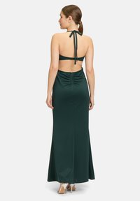 Langes grünes Kleid mit gerafft rückseitig und Halterneck. Glattes Material mit einem dezenten Glanz und funkelnden Akzenten an der Taille.