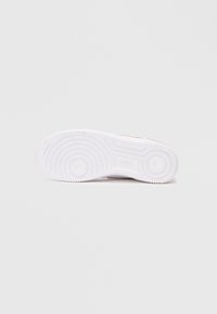 Sola de sneaker branca com padrão de pisada circular, apresentando borracha texturizada com sulcos e depressões para tração e aderência.