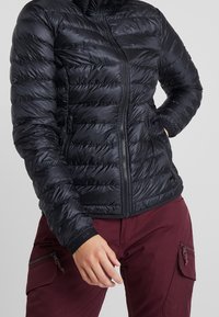 Svart puffjacka med kviltad design, framdragkedja och sidofickor. Tyget är slätt med en glänsande finish och en figurnära siluett.