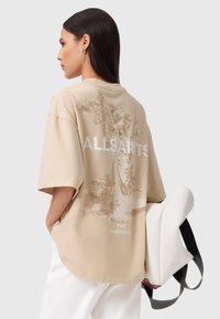 Beżowy, oversize t-shirt z graficznym nadrukiem na plecach, z napisem "ALLSAINTS LONDON" oraz ilustracją anioła. Materiał bawełniany.