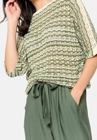 Grön och krämfärgad stickad topp med öppen vävdesign, prydd med horisontella ränder. I kombination med högmidjade gröna byxor med knyt.