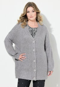 Grå stickad cardigan med djup V-ringning, sex knappar framtill och ribbade ärmslut. Bärs över en svart och vit mönstrad topp.