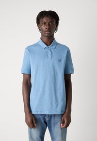 Camisola polo azul claro feita de tecido texturizado, apresentando um decote com colarinho, pala de dois botões e um pequeno emblema no peito.