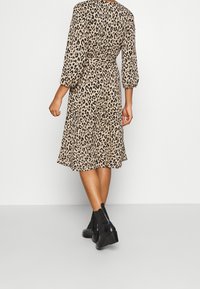 Šaty s leopardím potiskem, délka ke kolenům, se 3/4 narušenými rukávy, úzkým pasem a splývavou sukní. Nosené s černými kotníkovými botami. Hladká textilie.