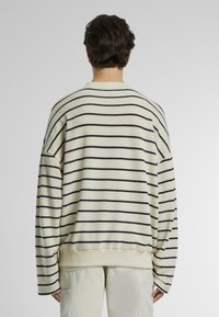 Felpa a righe con base crema e strisce orizzontali blu navy, spalle scese e vestibilità rilassata. Tessuto morbido.