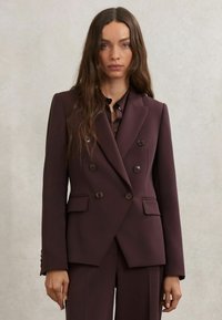 Dviejų eilių bordo spalvos švarkas iš lygaus audinio su priekinėmis kišenėmis su atvartais ir tamsiais mygtukais, derinamas su tokios pat spalvos marškiniais po apačia.