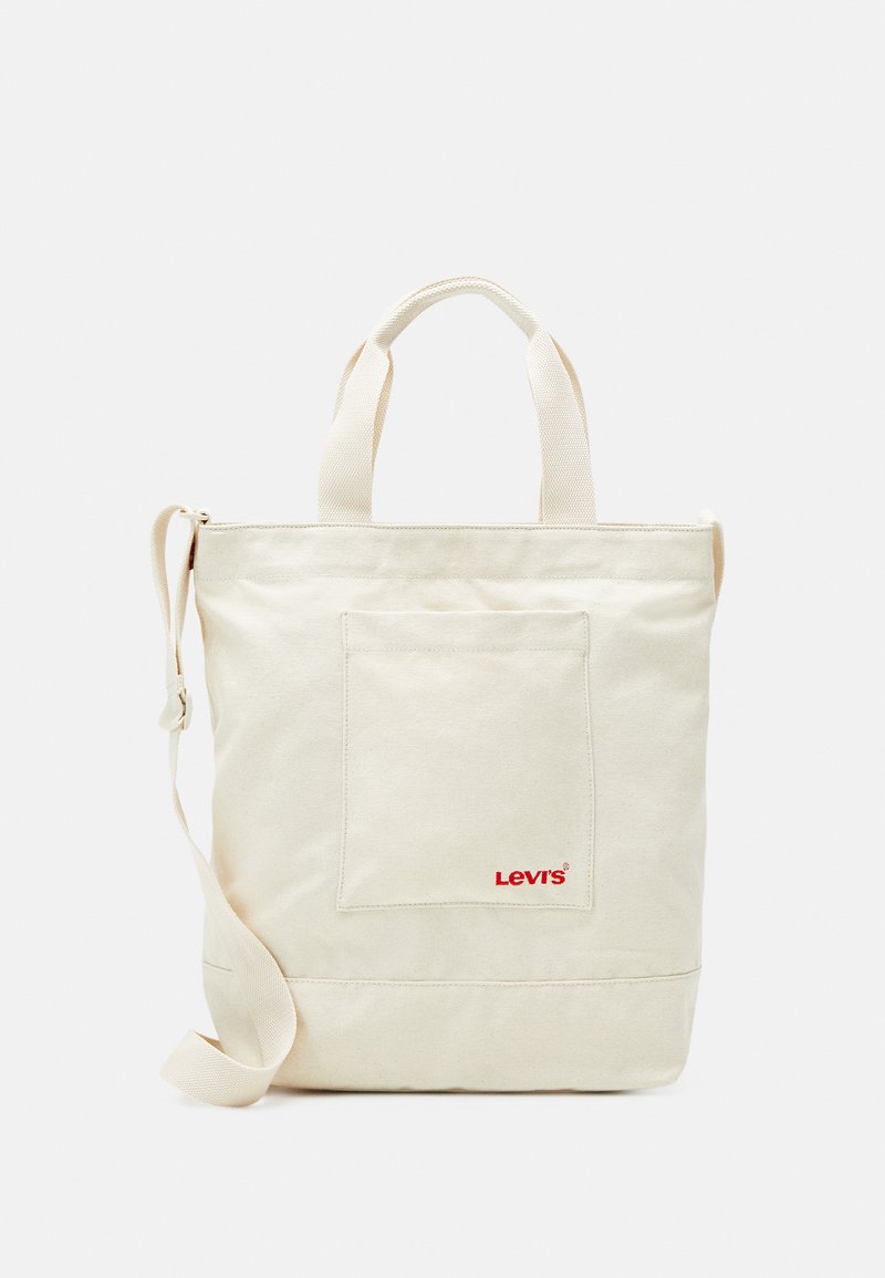 Cream-colored canvas tote bag with two top handles, shoulder strap, front pocket, and red Levi's logo. Smooth texture, rectangular shape.