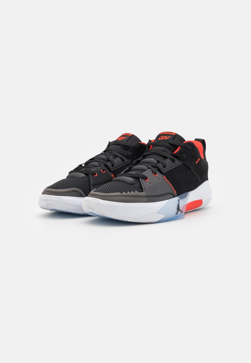 Chaussures de sport noires avec des accents rouges, en mesh et en matériau synthétique, fermeture à lacets, col rembourré et semelle extérieure translucide blanche.