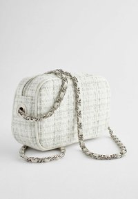 Witte tweed handtas met een gestructureerd ontwerp, voorzien van een zilveren kettingriem en een ritsluiting. Textuurstof en ronde hoeken.