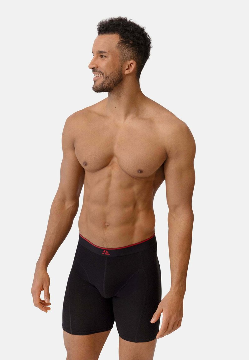 Svarte boxerkalsonger med röd midjeresår, med en åtsittande design och en slät tygstruktur, lämpliga för komfort och stöd.