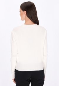 Biały sweter prążkowany z długimi rękawami i okrągłym dekoltem. Dół jest lekko skrócony, o gładkiej, miękkiej fakturze.