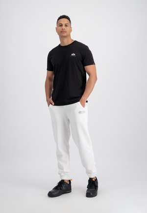 Sort kortærmet t-shirt med et lille logo, parret med hvide sweatpants med opfoldede ben, der har et brandnavn. Båret med sorte sneakers.