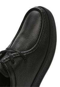 Chaussure en cuir noir à lacets avec dessus texturé, bout arrondi et semelle épaisse en caoutchouc, vue en gros plan sous un angle élevé.