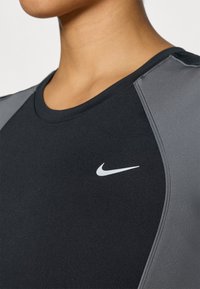 Μαύρο αθλητικό τοπ με γκρι λεπτομέρειες. Διαθέτει στρογγυλή λαιμόκοψη, ομαλή υφή και εξέχον λευκό λογότυπο Nike στο στήθος.