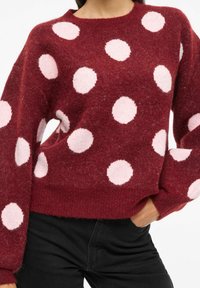 Jersey burdeos con grandes lunares rosas. Textura suave, corte relajado y mangas anchas. Combinado con pantalones negros.