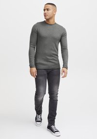 Gray long-sleeve shirt with a round neckline, paired with faded black slim-fit jeans and black and white sneakers. Simple, casual design.