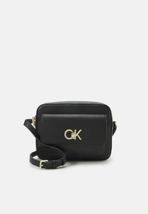 Sac bandoulière en simili cuir noir avec quincaillerie dorée, de forme rectangulaire, avec une poche à rabat à l'avant et une bandoulière ajustable. Logo CK affiché de manière proéminente.