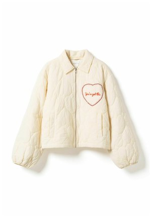 Krém színű steppelt dzseki elől cipzárral, két oldalzsebbel, elasztikus mandzsettákkal és a mellrészen egy "Mennek a dolgok" feliratú szív alakú folttal.