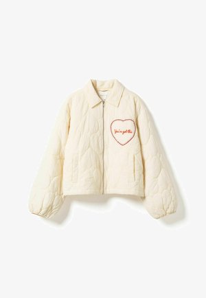 Cream quilted jacket with front zipper, two side pockets, elastic cuffs, and a heart patch reading "You've got this" on the chest.