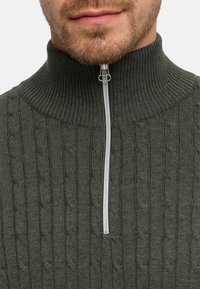 Zielony sweter dziany z wysokim kołnierzem i suwakiem sięgającym do jednej czwartej wysokości. Charakteryzuje się teksturowanym wzorem warkocza i srebrnym suwakiem.
