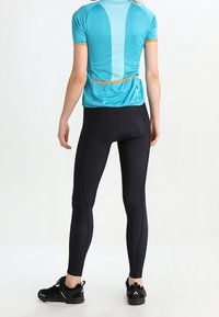Conjunto deportivo que presenta una camiseta ajustada de manga corta en turquesa con leggings negros. La camiseta tiene acentos en naranja y un bolsillo trasero.