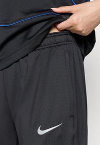 Sorte idrettsshorts laget av teksturert stoff med elastisk midje og sølvfarget Nike-logo på benet. Blå detaljer synlige nær livet.