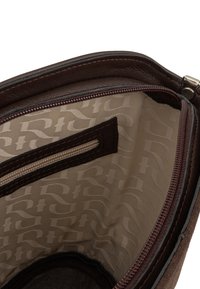 Interno di una borsa a tracolla in pelle marrone, con una fodera a motivo beige e una tasca con zip aggiuntiva, cuciture visibili e superficie liscia.