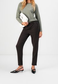 Pantalon noir sur mesure, pull en maille gris, tenant une pochette blanche. Talons slingback noirs pointus. Textures lisses et coupe ajustée.