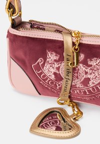 Borsa a tracolla in velluto rosa e bordeaux con hardware dorato, caratterizzata da un logo impresso, una catena in metallo e un charm a forma di cuore con specchietto.
