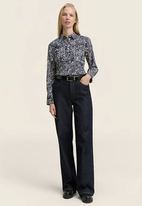 Navy patterned button-up shirt with long sleeves, paired with high-waisted dark denim trousers and a black belt. Black shoes complete the look.