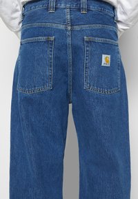 Siniset farkut, joissa on kaksi takataskua; oikeassa taskussa on pieni keltainen Carhartt-logopatch.