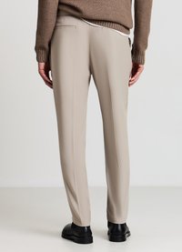 Beige maßgeschneiderte Hose mit glatter Textur, ausgestattet mit zwei Gesäßtaschen und schmalem Schnitt, kombiniert mit schwarzen Schuhen.