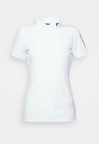 Vit polo skjorta tillverkad av glatt tyg, med en krage, femknappslå, och svart logotyp på vänster axel. Korta ärmar.