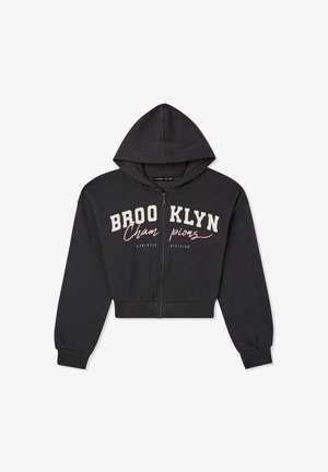 Przycięta ciemnoszara bluza z kapturem na suwak z napisem "BROOKLYN", połączona z jasnoniebieskimi spodniami cargo i czarnymi balerinami. Luźny krój, elastyczne mankiety.