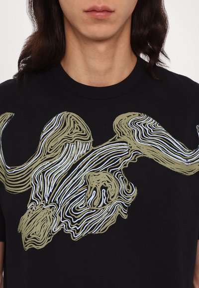 T-shirt en coton noir avec un design graphique d'un crâne de taureau dans des tons terreux, agrémenté de lignes blanches et bleues, créant un effet de texture superposée.