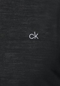 Black fabric with a textured finish featuring a small, embroidered white "ck" logo on the lower right. Simple and minimalist design.
