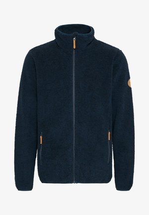 Jūrininkų mėlynas švarkas iš fliso su aukštu apykakle, priekine užtrauktuku ir odiniais akcentais kišenėse. Minkšta, tekstūruota medžiaga su laisvu siluetu.