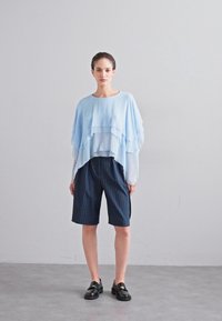 Lichtblauw gelaagd blouse met vloeiende stof, gecombineerd met donker gestreepte knieboller en zwarte instapschoenen.