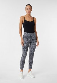 Top nero senza maniche abbinato a leggings aderenti con stampa leopardata grigia e nera, indossato con scarpe da ginnastica bianche. Texture liscia in tutto.