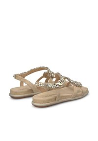 Sandalias planas beige con correas decorativas de strass, material texturizado similar a ante y una suela metálica sutil. Diseño de perfil bajo para mayor comodidad.