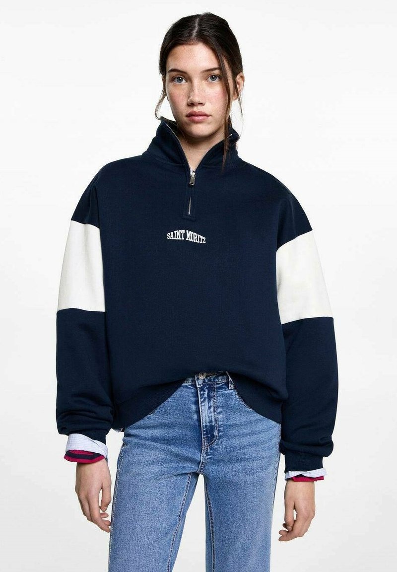 Pull en marine avec manches blanches, fermeture éclair sur le devant, broderie "SAINT MORITZ", tissu doux, coupe décontractée, détails de poignets côtelés.