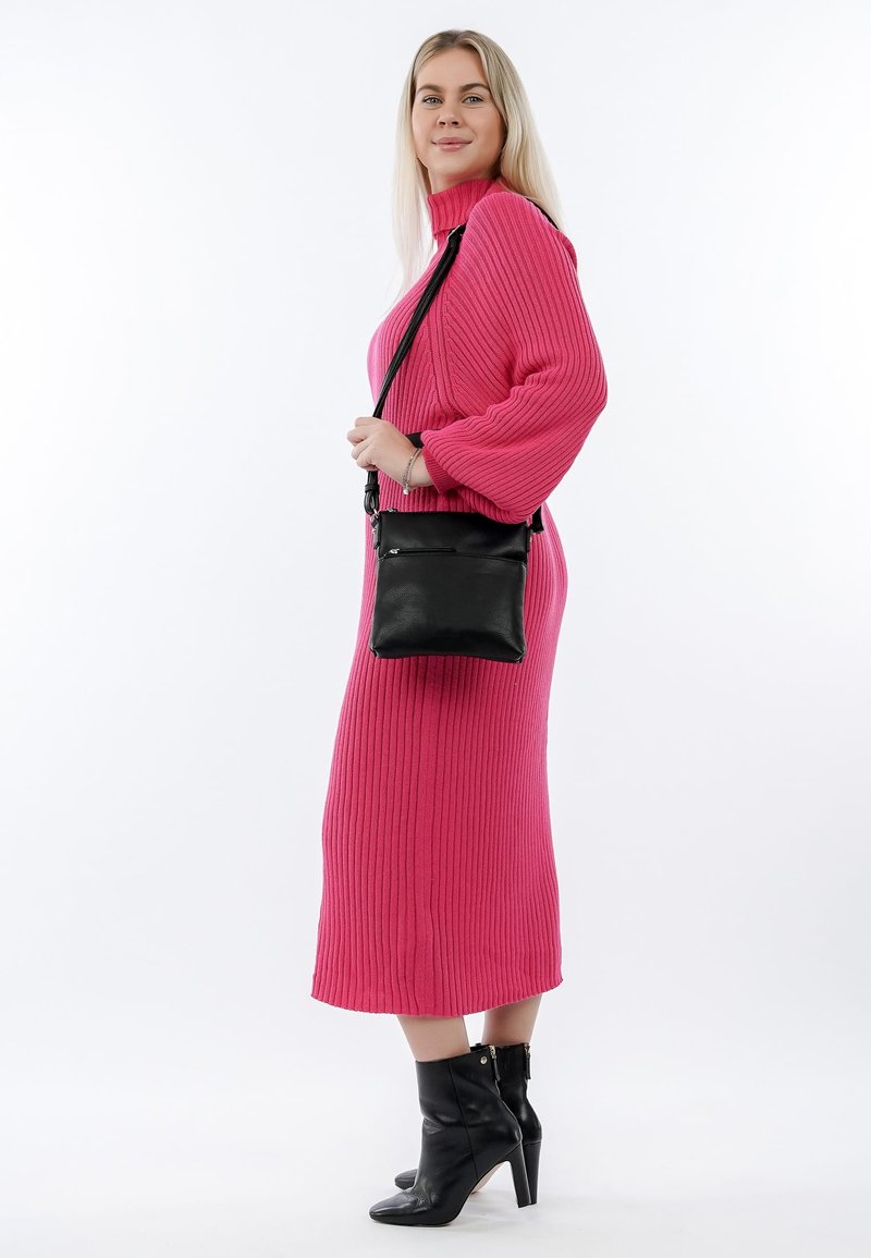 Sort læder crossbody taske med en lynlåslomme på forsiden, båret med en lyserød ribbet kjole og sorte hælede ankelsko.