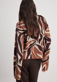 Stickad tröja med ett mönster av bruna, beige och krämfärgade vågor, med en avslappnad passform och vida ärmar. Texturerat tyg, beskuren längd.