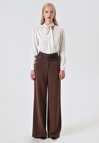 Witte blouse met een gestrikt halsdetail, gecombineerd met hooggevoerde, wijde bruine broek en een dubbele riemaccent. Glad materiaal en gestructureerde pasvorm.
