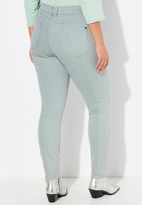 Vaqueros ajustados de un azul claro con una cinturilla elástica, bolsillos traseros y detalles de costura sutil, combinados con botas de tacón metálico hasta el tobillo.