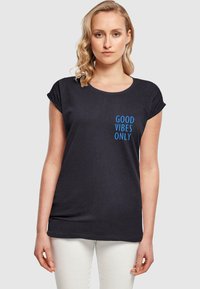 Sort kortærmet t-shirt i bomuld med blå tekst "GOOD VIBES ONLY" på venstre side. Glat tekstur, afslappet pasform.