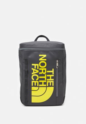 Czarny prostokątny plecak z górnym uchwytem, przednią kieszenią na zamek oraz dużym żółtym logo "THE NORTH FACE" na przednim panelu.