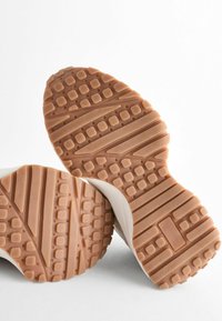 Sneakers med en texturerad gummisula, med en beige färg, rutmönster och slätt vitt övre material.